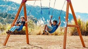 Two children on a wooden swing set in a grassy field with mountains in the background. -  Dells treetop lakeside lodging on famous Canyon Road. A top location! (Wisconsin Dells)