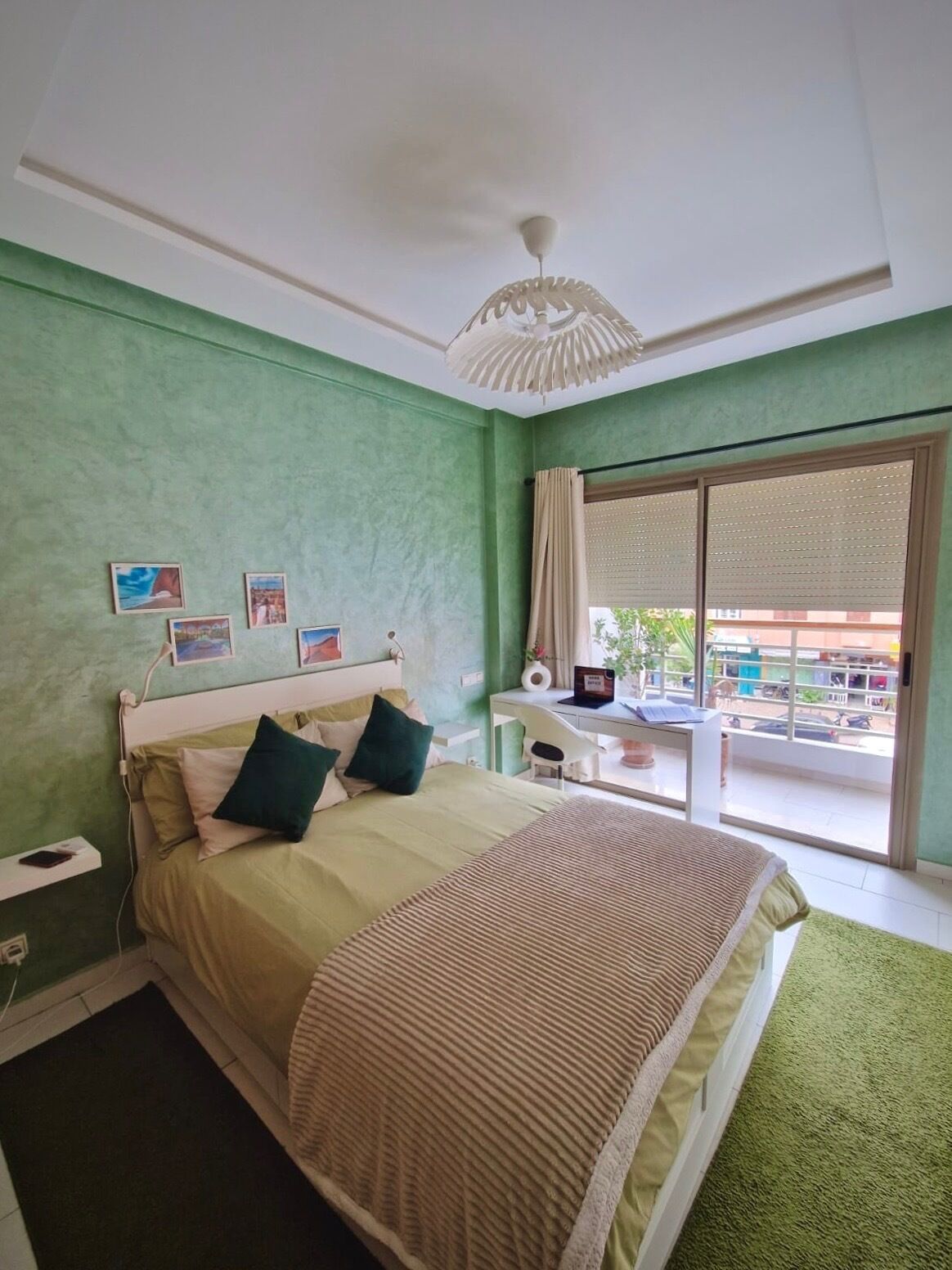 A bedroom with a bed, a desk, and a view of the outside.