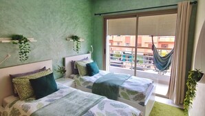 Une chambre avec deux lits, un mur vert, un ventilateur de plafond et une vue sur l’extérieur.