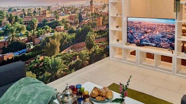 Un salon avec une fresque représentant un paysage urbain, un téléviseur à écran plat, une table basse avec des collations et des plantes suspendues.