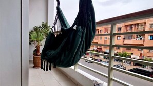 Un balcon avec un hamac, une plante en pot et une table où sont disposés des croissants et du café.