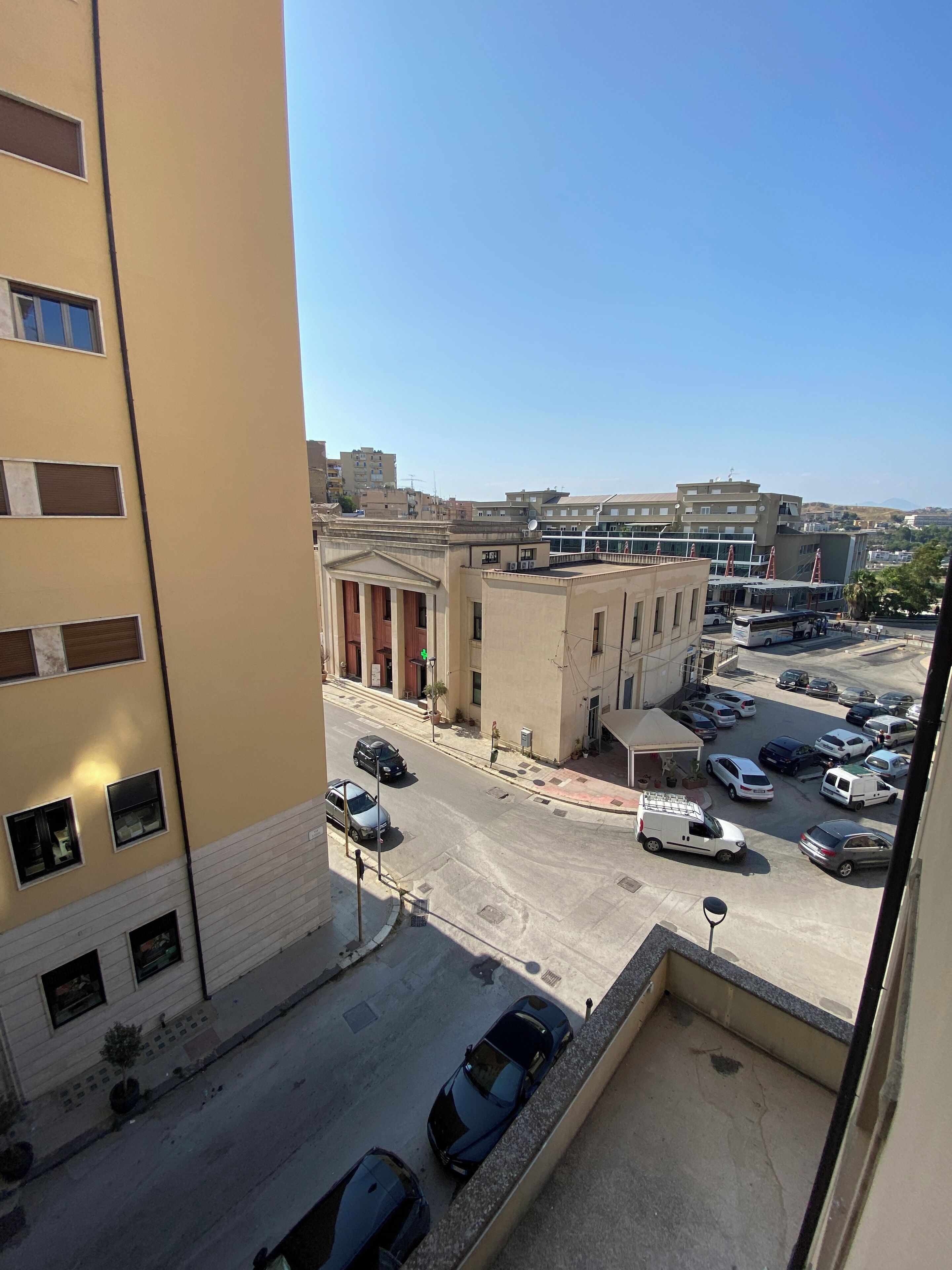 A view of a parking lot with several cars, a building with columns, and a clear sky.