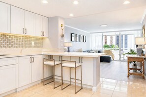 Une cuisine moderne avec des meubles blancs, un pare-feu en marbre et un coin bar équipé de tabourets.