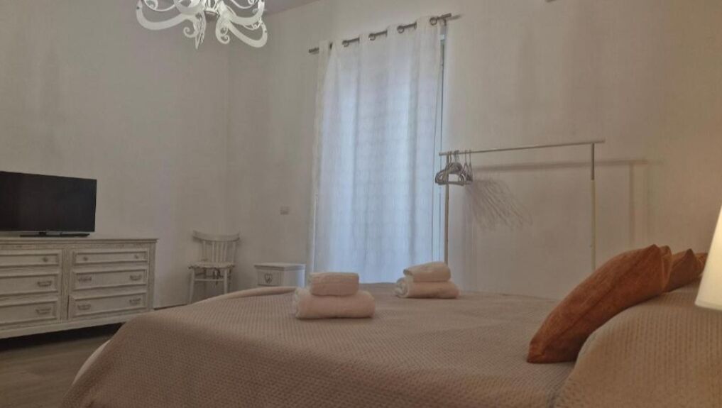 A bedroom with a bed, a television, a dresser, a chair, and a window with curtains.