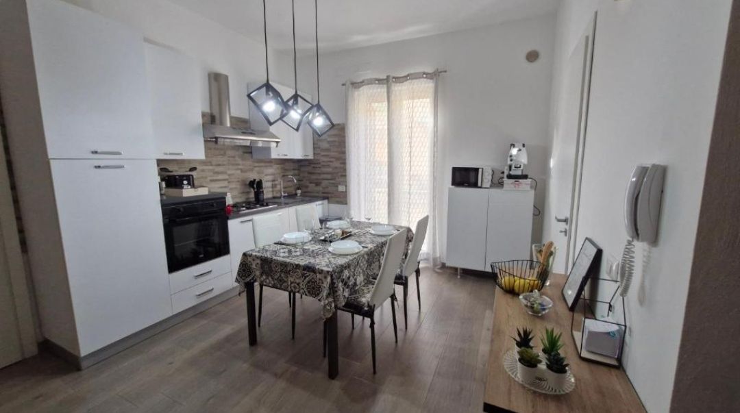 Una cucina moderna con mobili bianchi, un tavolo da pranzo per quattro persone e un forno integrato.