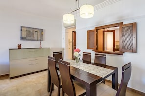 A dining area with a table, chairs, a vase with flowers, and a cabinet. - Sea-view Apartment With Pool (Ayamonte)