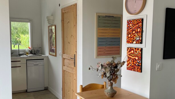 A dining area with a wooden table and chairs, a vase with dried flowers, and a clock on the wall.