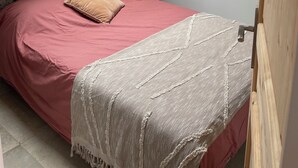A bedroom with a skylight, a bed with a red bedspread, a patterned headboard, a nightstand with a lamp, and a wooden door.
