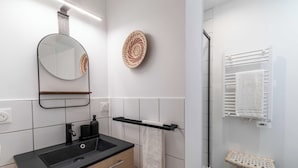 Un baño moderno con lavamanos negro, mueble de madera, espejo, toallero y un taburete pequeño.