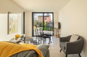 Una sala moderna con un sofá, un sillón gris, una mesa de comedor con sillas y un amplio ventanal corredizo que da a un patio exterior.