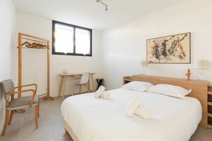 Quarto de hotel com cama, escrivaninha, cadeira, guarda-roupa e janela.