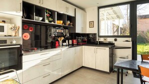 A modern kitchen with white cabinets, black appliances, and a large window providing natural light. - Dify Stoppa - Parilly (Venissieux)