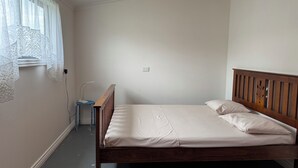 A single-bed room with a wooden headboard, a bedside table, and a power outlet on the wall. - A cosy sleep out in backyard (Kennington)