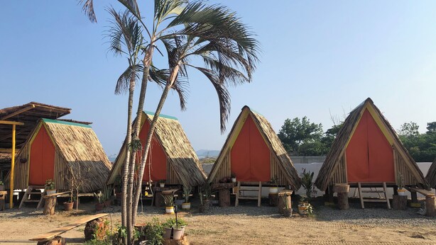 A row of thatched-roof huts with a sandy ground and potted plants around them. - Modern Duplex 2-Bedroom Apartment with Sea View of Baroro Beach. (Bacnotan)
