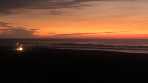 A beach at sunset with a distant light source, likely a lighthouse or beacon, and a clear sky with clouds. - Modern Duplex 2-Bedroom Apartment with Sea View of Baroro Beach. (Bacnotan)