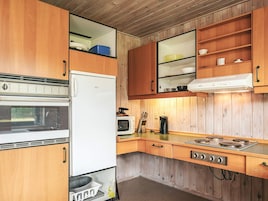 A compact kitchen with wooden cabinets, a white refrigerator, a microwave, and a gas stove.