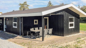 Ein schwarzes Metallgebäude mit überdachter Terrasse, einem kleinen Tisch mit Stühlen und einem Fenster.