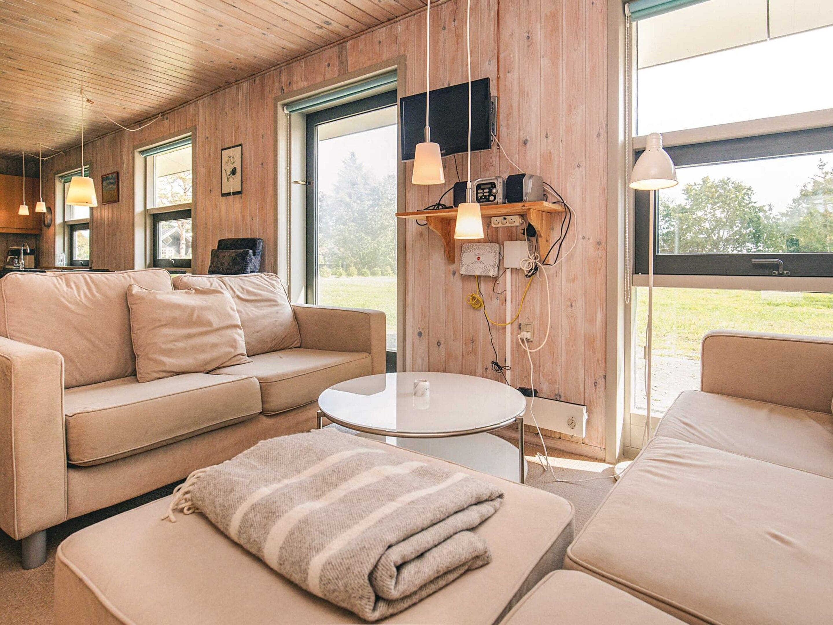 A cozy room with a sofa, a small table, and a bench. There are wooden walls and a large window.