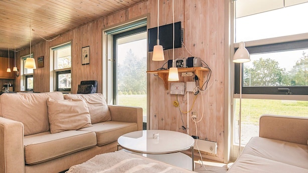 Ein gemütliches Zimmer mit Holzvertäfelung, einem Sofa, einem kleinen runden Tisch und einem Fenster mit Blick ins Freie.