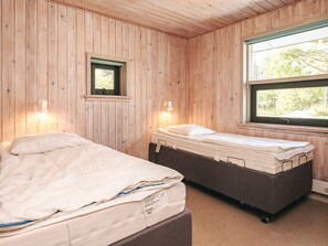 A room with two beds, wooden walls, a window, and a small window with a view of trees.