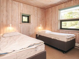 Una habitación con dos camas, paredes de madera, un ventanal y un pequeño ventanillo con vista a árboles.