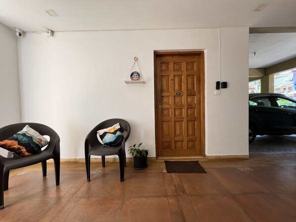 A clean, modern interior with a wooden door, a black chair with a colorful cushion, and a potted plant. - Goan Hideaway - Uno (Siolim)