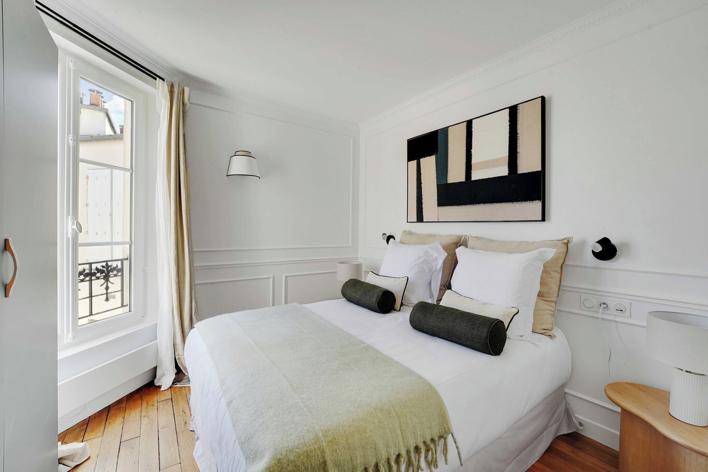 Un dormitorio con cama, ventana, un cuadro y una mesita de noche.