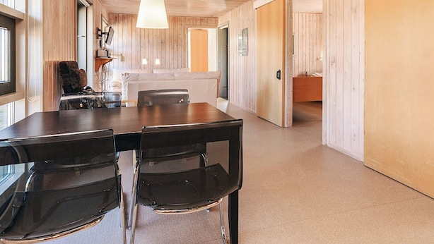 A modern interior with a wooden ceiling, a dining area with a table and chairs, and a kitchen visible through an open door. - 4 Person Holiday Home in Hals (Hals)