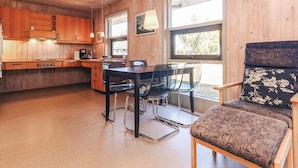 A cozy cabin interior with wooden walls, a dining area with a table and chairs, a kitchen with wooden cabinets, and a large window providing natural light. - 4 Person Holiday Home in Hals (Hals)