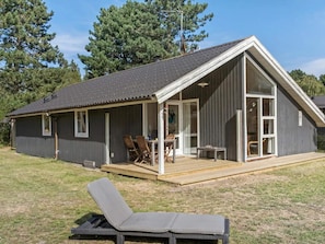 A single-story building with a covered porch, a sliding glass door, and a small outdoor seating area with chairs and a table.