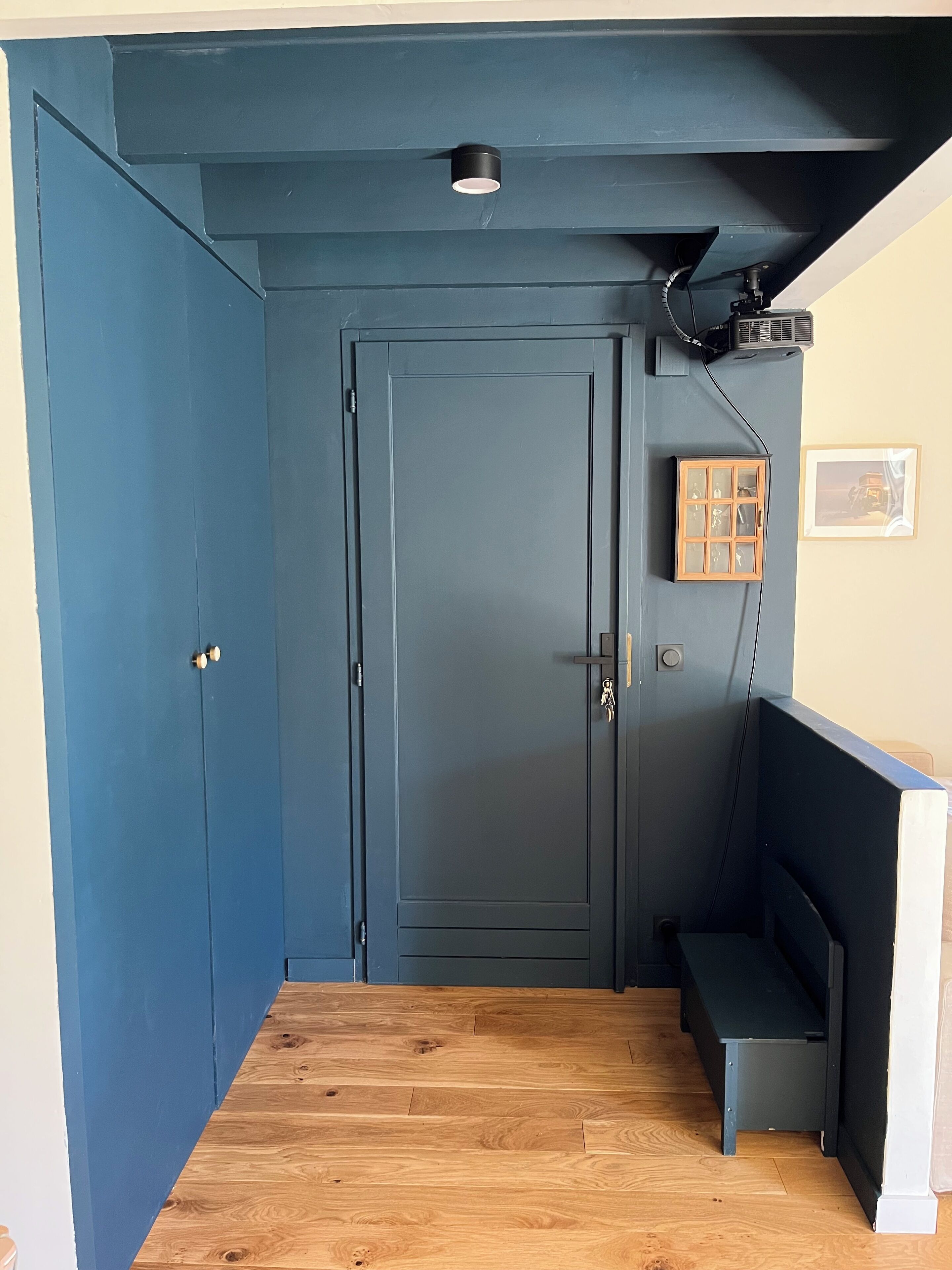 A hallway with a dark blue door, a small bench, and a framed picture on the wall.