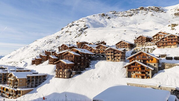 Een met sneeuw bedekte berglodge met meerdere houten gebouwen, skipistes en een heldere lucht.