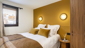 Hotelkamer met een bed, twee bedlampen, een nachtkastje en een raam met uitzicht op gebouwen.