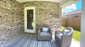Une terrasse couverte avec des murs en briques, deux fauteuils en osier dotés de coussins et un tapis à rayures.