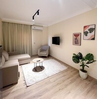 A modern living room with a sofa, a small round table, a potted plant, and artwork on the wall.