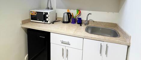 A compact kitchen with white cabinets, a built-in dishwasher, a sink, and a window above the countertop.