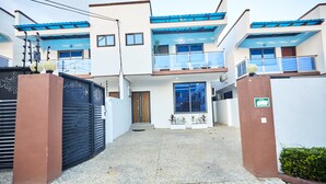 A modern two-story house with a gated entrance, a balcony on the upper floor, and a small garden area. - 3-bedroom 3.5-ba house in a gated community in Accra with AC. Family-friendly (Kwabenya)