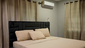 A bed with a black headboard, beige bedding, and beige curtains. - 3-bedroom 3.5-ba house in a gated community in Accra with AC. Family-friendly (Kwabenya)