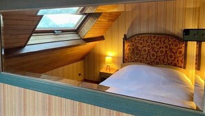 A bedroom with a sloped ceiling, a skylight, a patterned headboard, a bedside lamp, and a bed with white bedding. - Vacation home in Le Pouliguen - Pets welcome! (Le Pouliguen)