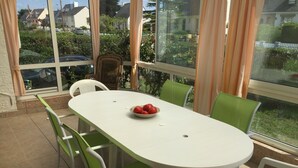 A dining area with a white table and green chairs, a wicker chair, and a bowl of tomatoes on the table. - Vacation home in Le Pouliguen - Pets welcome! (Le Pouliguen)