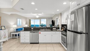 Una cocina moderna con armarios blancos, electrodomésticos de acero inoxidable y un amplio ventanal con vista al océano.
