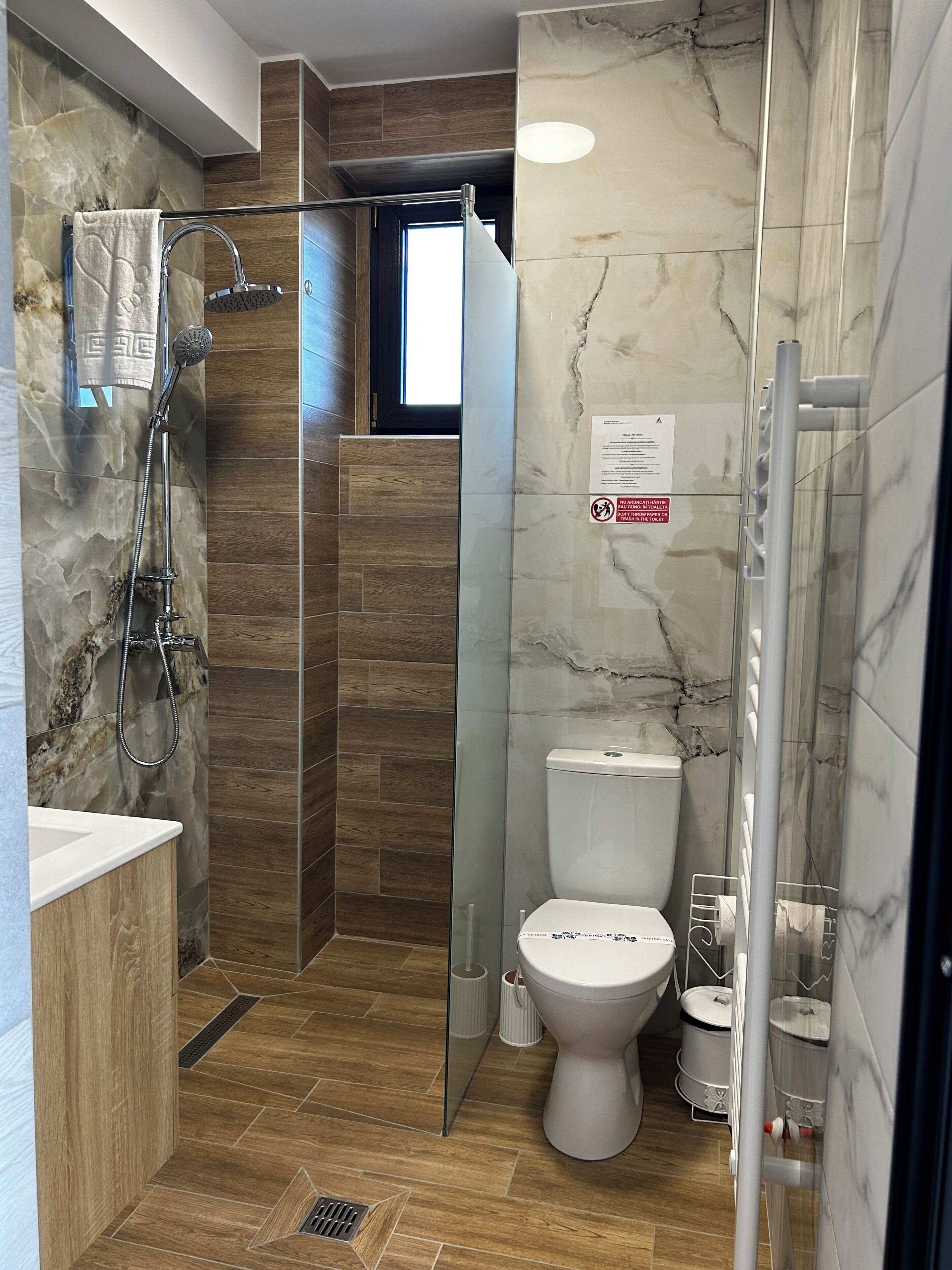 Un baño moderno con ducha, inodoro y lavamanos, con paredes de mármol y suelo de madera.