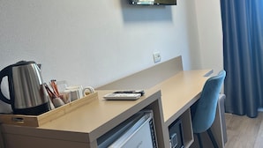 Een compacte hotelkamer met kitchenette, een flatscreen televisie aan de muur en een raam met gordijnen.