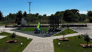 Een verhard pad dat leidt naar een speeltuin met schommels en een glijbaan.