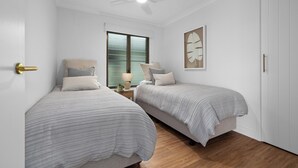 A bedroom with two beds, a ceiling fan, a window with blinds, and a wall-mounted artwork. - Sundaze at Kingy Creek (Kingscliff)