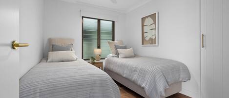 Ein Schlafzimmer mit zwei Betten, einem Deckenventilator, einem Fenster mit Jalousien und einem Wandbild.