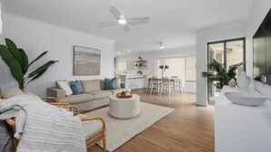 A spacious living room with a white sofa, a round coffee table, and a large plant. - Sundaze at Kingy Creek (Kingscliff)