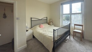 A bedroom with a bed, a nightstand, a chair, a window, and a chandelier.