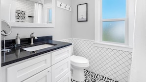A bathroom with a white toilet, a black and white patterned floor, a black countertop sink, and a window with a view of the sky.