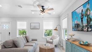 A modern living room with a grey sofa, a round wicker ottoman, a teal cabinet, and a ceiling fan.